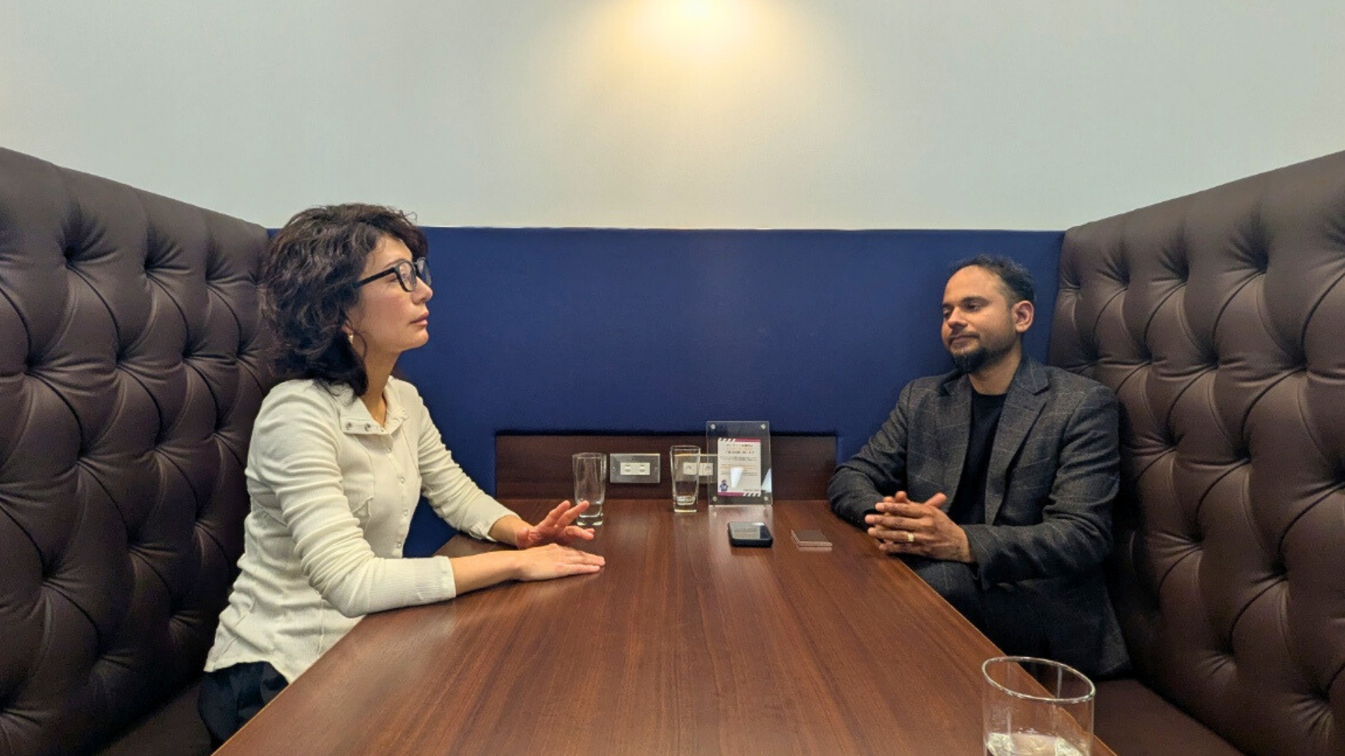 個室ブースのテーブル席で、真剣な表情で対面して会話をする大野とニティッシュ